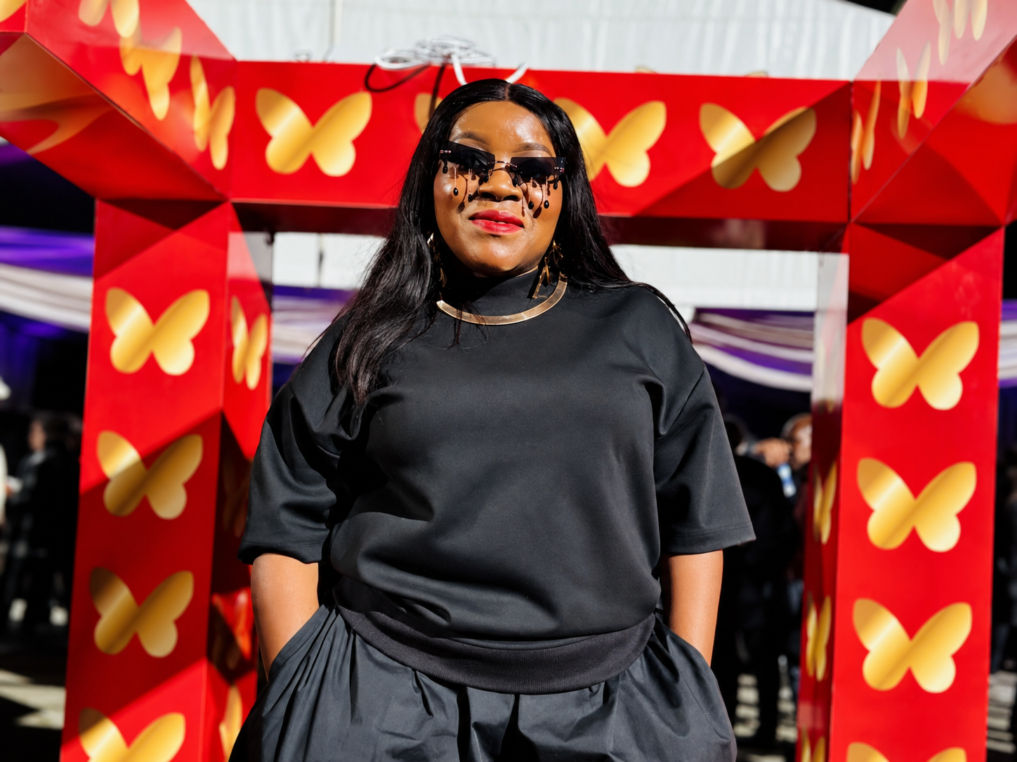 Guest in black standing in front of a red butterfly-branded event arch